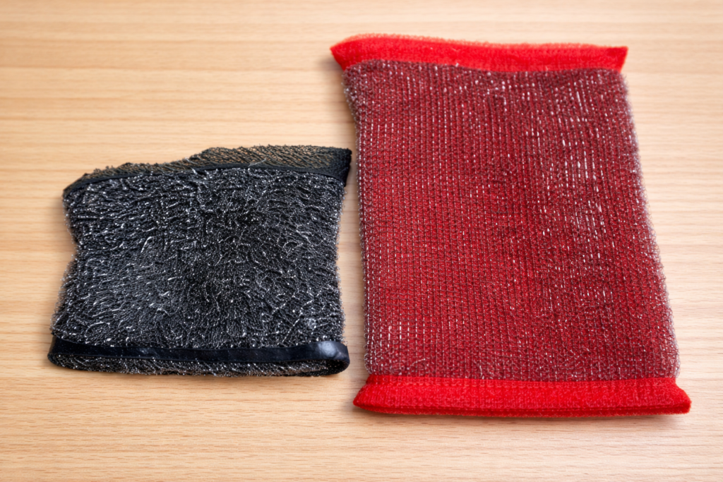 木目のテーブルの上に並べた黒と赤の金属メッシュスポンジの写真。サイズの違いが分かるように横並びで置かれている。