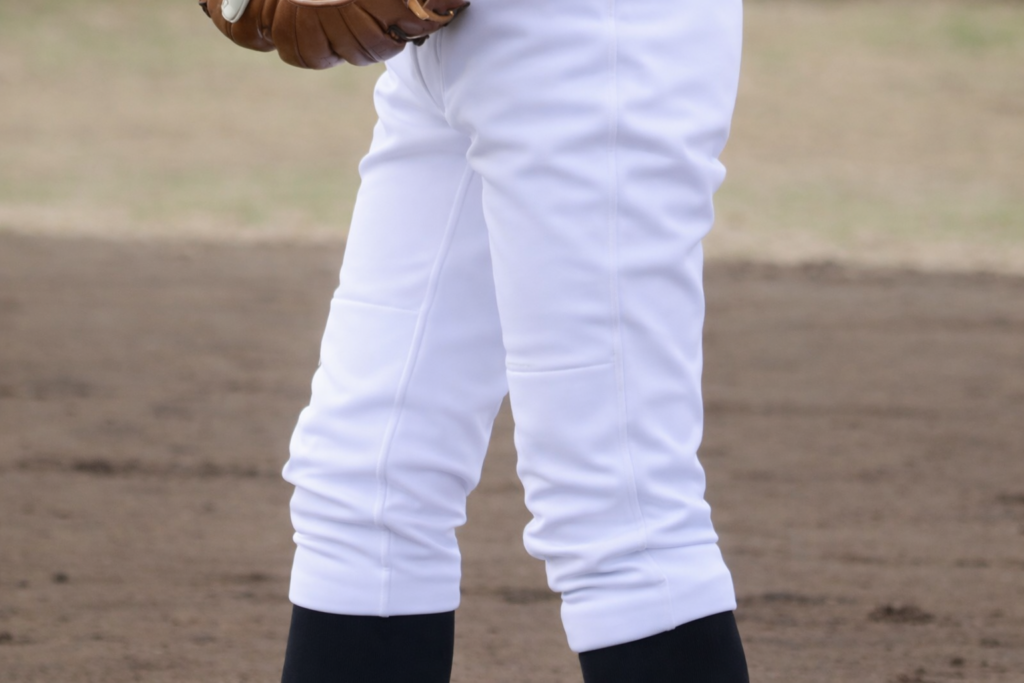 屋外のグラウンドで立つ選手の下半身。泥汚れが落ちて真っ白になった野球ユニフォームのズボンと黒いソックスが見える様子。