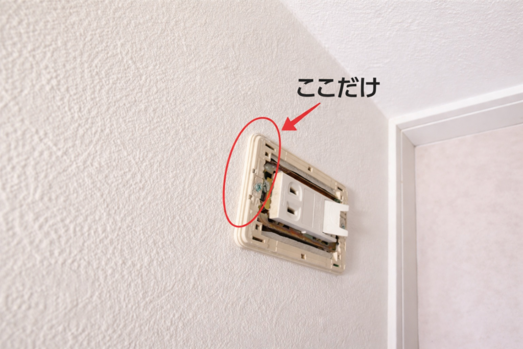 壁のスイッチカバーの角を赤い楕円で強調し、矢印と「ここだけ」と書かれた注釈が付いた写真