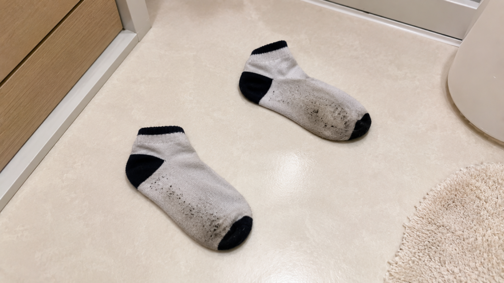 泥や砂汚れが付いた子ども用の靴下が、洗面所の床に脱ぎっぱなしで置かれている様子